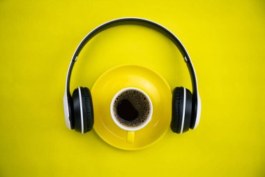 Sarı kağıt arka planda kulaklıklı Yellpw kahve fincanının en üst görüntüsü