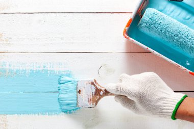 Tekerlekli fırçayla fırçayı tutan adamın eli beyaz ahşap duvarda mavi boya.