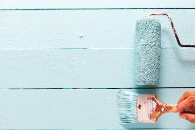 Tekerlekli fırçayla fırçayı tutan adamın eli mavi ahşap duvarda mavi boya.