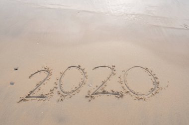 Deniz dalgası 2020 'yi silip süpürüyor. Beyaz kumlara yazı yazıyor. Plajda güzel bir gün doğumu ve kumlu sahile vuran dalgalar.