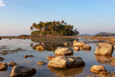 Tropikal deniz günbatımında küçük bir ada ya da gelgit gününde gün doğumu.