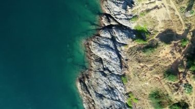 Mavi bir okyanustaki deniz kıyısı kayalarının tepesindeki hava aracı kamerası. Deniz dalgaları güzel deniz manzaralı insansız hava aracı 4k. Yüksek kalitede okyanus dalgaları boş kaya kayalıklarına çarpıyor.