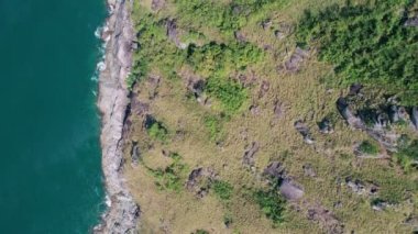 Mavi okyanusun yukarısındaki kayalıklara çarpan tropikal denizin yukarıdan aşağıya doğru uzanan dalgalı görüntüsü. Güzel deniz yüzeyi hava görüntüsü drone görüntüsü, yüksek açılı andaman görüntüsü.