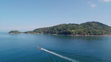 Yukarıdan göz kamaştırıcı bir hava kamerası görüntüsü uçuyor. Turistlerle dolu uzun kuyruklu bir tekneyi takip ediyor. Mavi denizde yelken açıyor.