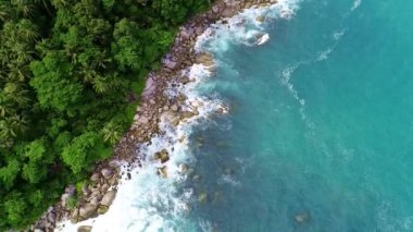 Dev okyanus dalgalarının tepesinden aşağıya doğru inen muhteşem hava manzarası tropikal denize çarpıyor ve köpürüyor. Büyük kaya taşlarıyla güzel deniz kıyıları. Kuş gözü deniz manzarası ve dağ tepesi ormanı.