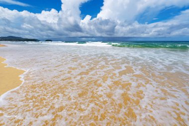 Muhteşem kumlu kumlu sahil dalgalı deniz köpüğü kumlu kıyı turkuazında çarpışıyor okyanus suyu ve mavi gökyüzü beyaz bulutları denizin üstünde yaz tatili için doğal arka plan seyahat web sitesi.