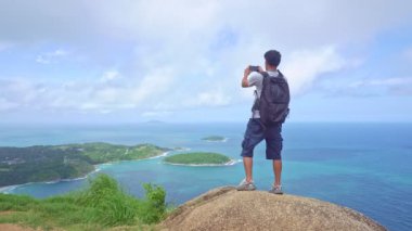 Sırt çantalı genç adam Phahindum bakış açısına göre Phuket Tayland 'da popüler bir noktada duruyor ve akıllı telefon ile video ve fotoğraf çekiyor tatil seyahati kavramı Phuket Tayland