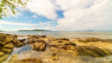 Sabah bulutlu açık mavi gökyüzünün altında kayalık deniz kıyısı ve yapraklar arka planda Güzel deniz ve Phuket Tayland 'da küçük ada