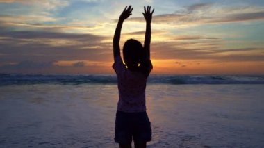 Siluet Asyalı genç kız 7 yaşında plajda gün batımında duruyor plajda kollarını kaldırıyor yaz tatili günbatımının ya da gün doğumunun tadını çıkarıyor mutluluk yolculuğu ve mutluluk konsepti videosu.