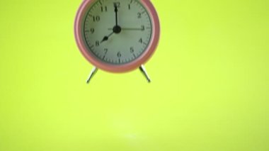 El Asyalı erkek, sarı masa üzerindeki çalar saati seçiyor. Stüdyoda, sarı arka planda izole edilmiş.