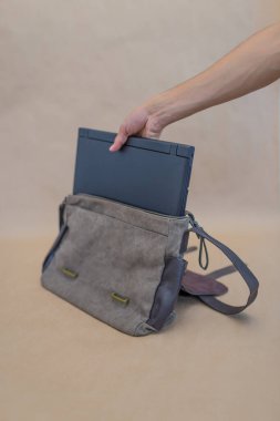 Tanınmayan birinin bej bir arkaplan üzerine dizüstü bilgisayarı bez bir çantaya koyması.