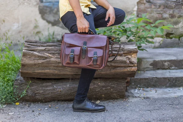 Man holding brown leather messenger bag in the hand. Unisex bag for sale.