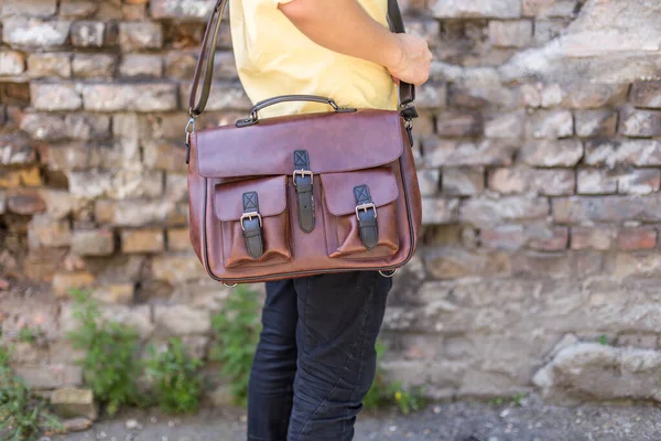 Man carries brown leather messenger bag in the hand. Unisex bag for sale.