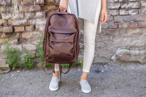 Woman holding brown leather backpacks in the hand. Unisex bag