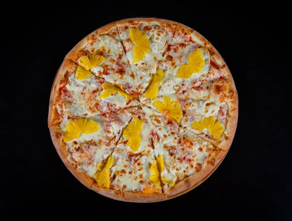 Top view of Hawaiian pizza topped with pineapple with chicken on mozzarella cheese on a thick pie crust on a black background