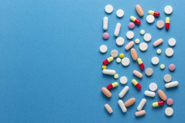Mavi arka planda bir sürü hap, vitamin ve kapsül var.