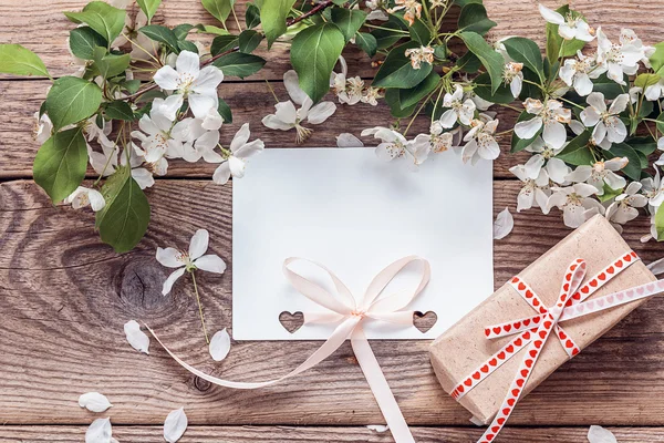 Λευκή κάρτα, άνθος μήλου και κουτί δώρου σε ξύλινο φόντο. Pla — Φωτογραφία Αρχείου