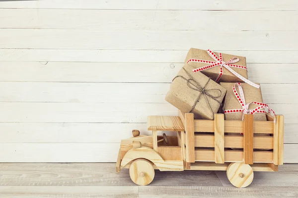 Wooden toy truck with gift boxes in the back on a white wooden b