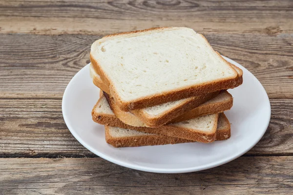 A stack of white bread slices on a plate on a wooden table. Stock Picture