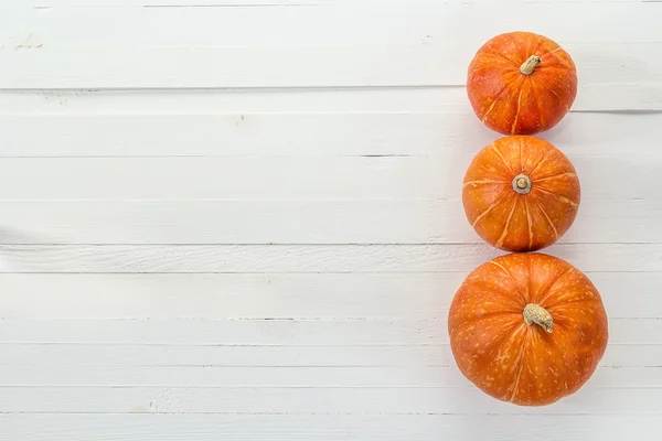 Achtergrond met drie pompoenen op een witte houten planken. Ruimte f — Stockfoto