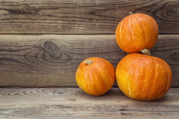 Drei orangefarbene Kürbisse auf einem Hintergrund aus alten Holzbrettern. — Stockfoto