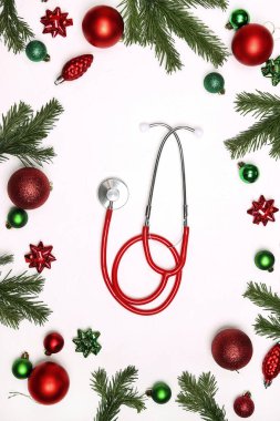 Beyaz arka planda Noel süslemesi olan kırmızı steteskop. Noel medikal yatağı. 