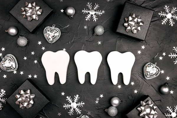 White teeth with silver decorations and gift boxes on black background. Dentist Merry Christmas and New Year concept. Top view, flat lay.
