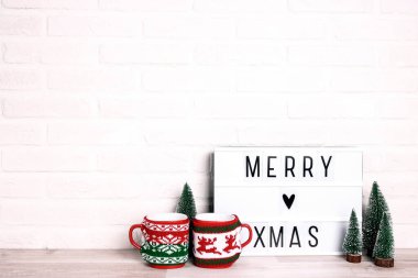Minyatür Noel ağaçları ve beyaz tuğla duvara dayanmış birkaç kupayla Mutlu Xmas mesajları. Metin için alanı kopyala.