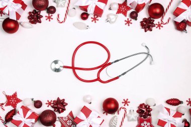 Beyaz arka planda Noel süslemesi olan kırmızı steteskop. Tıbbi kış tebrik kartı.. 