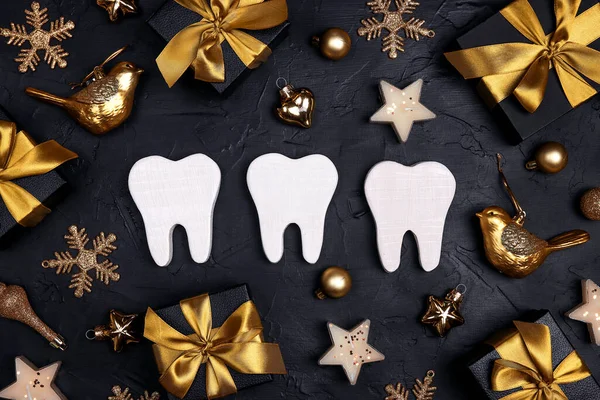 White teeth with gold decorations and gift boxes on black background. Dentist Merry Christmas and New Year concept. Top view, flat lay.