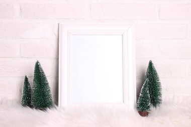 Beyaz tuğla duvara karşı minyatür köknar ağaçları olan boş beyaz çerçeve. Tasarım, harf ya da ifade için boşluk kopyala.