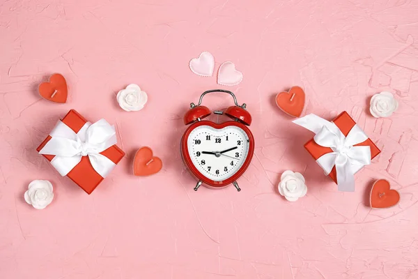 Heart shaped alarm clock with gift boxes, candles hearts and roses on pink background. Flat lay, top view Valentine\'s day concept. Time for love and greetings.