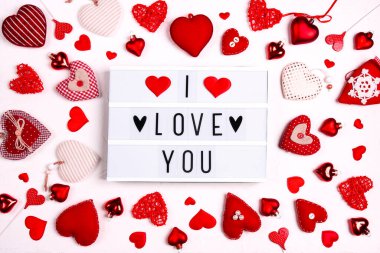 Beyaz ışıklı kutuda beyaz arka planda bir sürü farklı kalbi olan mesajını seviyorum. Sevgililer Günü kompozisyonu.