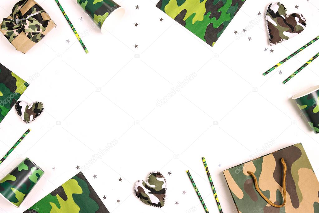 Festive frame for Defender of the Fatherland Day, February 23. Party set with camouflage glasses, straws, napkins and gifts on white background with copy space for text.