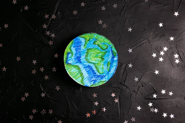 Drawn planet Earth among the stars on a black background. Science, ecology, environmental protection. World Earth Day concept.