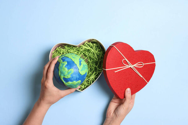 Female hands holding heart gift box with planet earth on a blue background. Earth Day, ecology and nature protect.