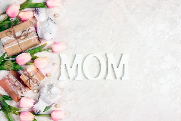 Festive border from tulip flowers, gifts and birds with word MOM on light marble. Mother's Day  greeting card.