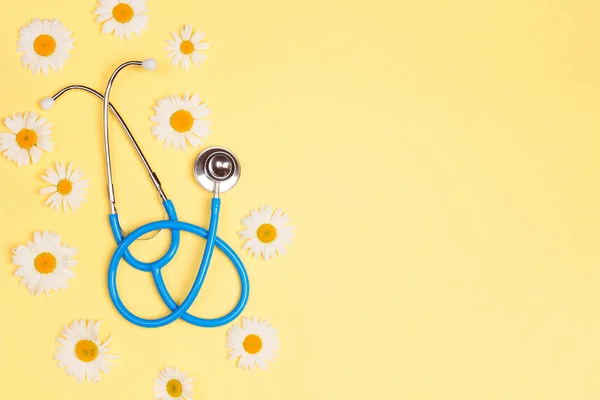 Blue stethoscope with chamomile flowers on yellow background. Top view with copy space. National Doctor\'s day. Happy nurse day.