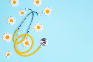 Mavi arka planda papatya çiçekleri olan sarı steteskop. Kopyalama alanı olan üst görünüm. Ulusal Doktor Günü. Mutlu hemşire günleri.. 