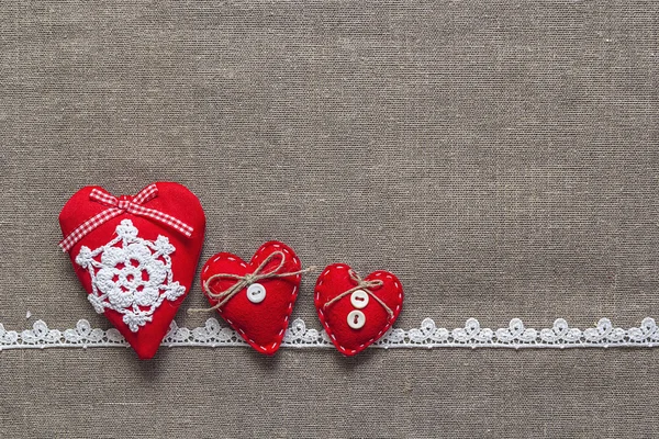 Tres corazones rojos y encaje sobre fondo de arpillera — Foto de Stock