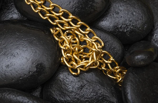 Golden color chain with black stones in background.