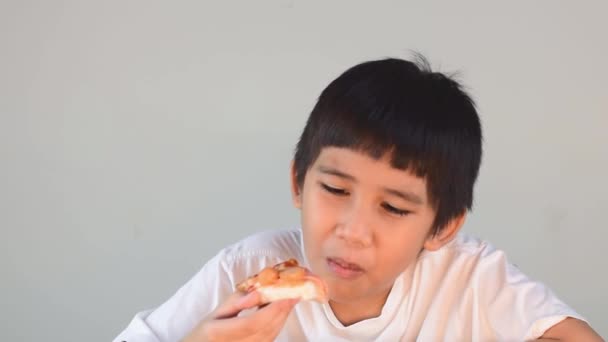 身穿白衬衫的亚洲可爱男孩快乐地坐在一起吃披萨 — 图库视频影像