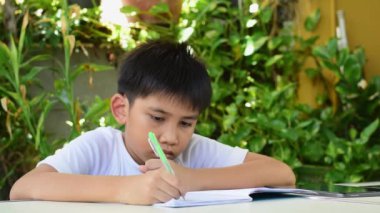 Asyalı çocuk ödevini bir deftere yazmak için kalem kullanarak yapıyor..