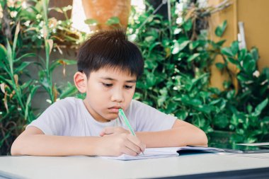 Asyalı çocuk ödevini kitap yazmak için bir kalem kullanarak yapıyor..