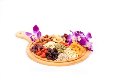 Beyaz arka planda izole edilmiş ahşap bir tabakta çeşitli kurutulmuş meyve grupları ve güzel orkidelerle kurumuş tahıllar..