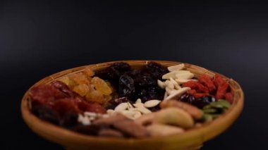 Siyah arka planda bambu tepsisinde çeşitli türde tahıl ve kurutulmuş meyve grupları..
