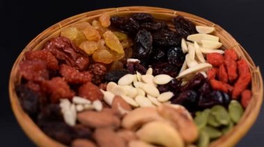 Siyah arka planda bambu tepsisinde çeşitli türde tahıl ve kurutulmuş meyve grupları..