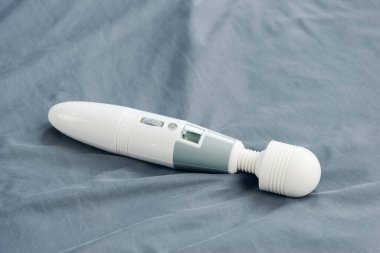 Kırışmış yatakta uzanan titreşimli seks oyuncağına yakın çekim.