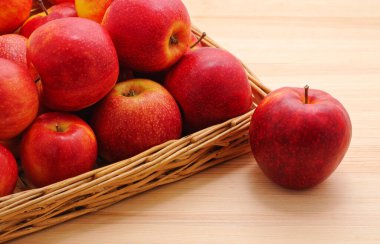 Bir elma ve bir grup kırmızı elma ahşap bir masada sepetin içinde.