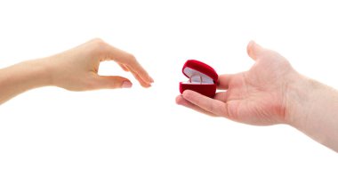 Bir erkek eli altın bir alyansla açık kırmızı kadife bir kalp kutusunu tutarken bir kadın eli ona uzanır, beyaz bir arka planda izole bir şekilde..